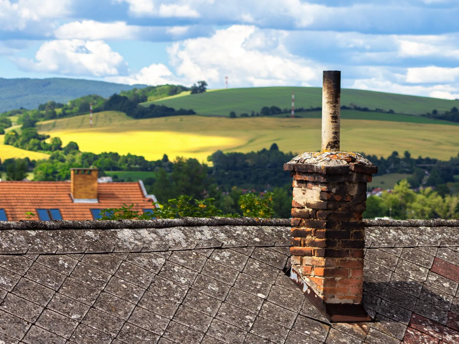 Weathered old brick chimney with crumbling mortar on a worn roof